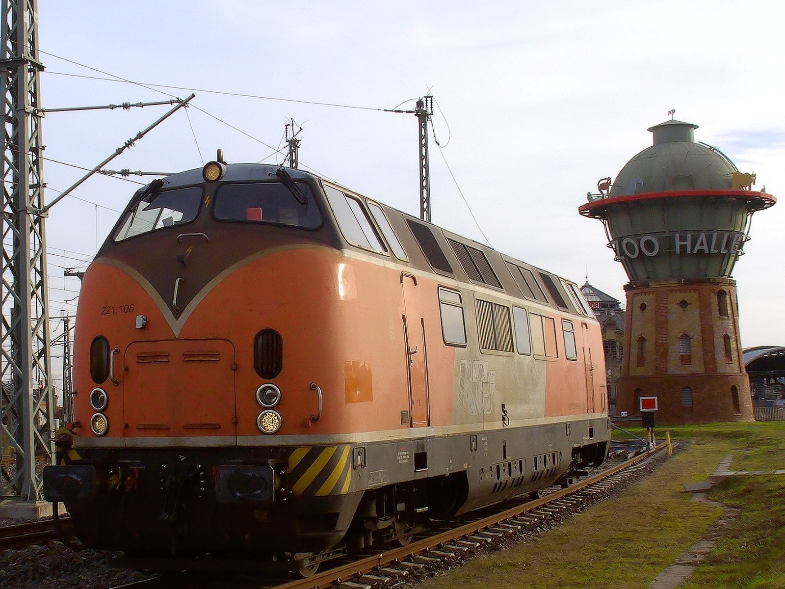 Bild in voller Größe in neuem Tab Schmutzige, orange Diesellok 221.105 von links vorn aufgenommen; hinter der Lok ist rechts im Bild der Wasserturm am Bahnhof Halle (Saale) zu sehen