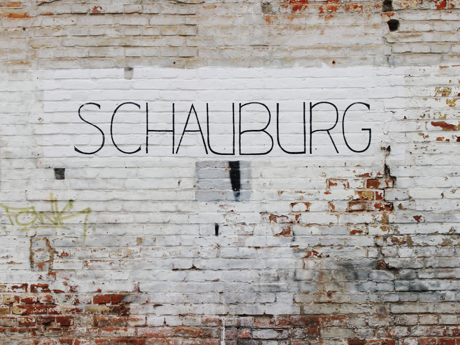 In dünnen schwarzen Großbuchstaben steht auf einem geweißten Bereich der Ziegelwand „SCHAUBURG”